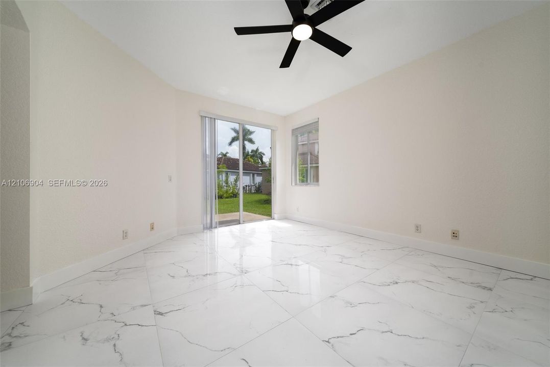 Interior space featuring large-format veined tile flooring, neutral wall tones, a black ceiling fan with integrated lighting, and a sliding glass door