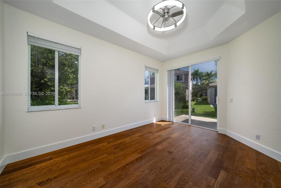 Tray ceiling with integrated circular lighting, wood-finish flooring, and sliding glass door access to the exterior