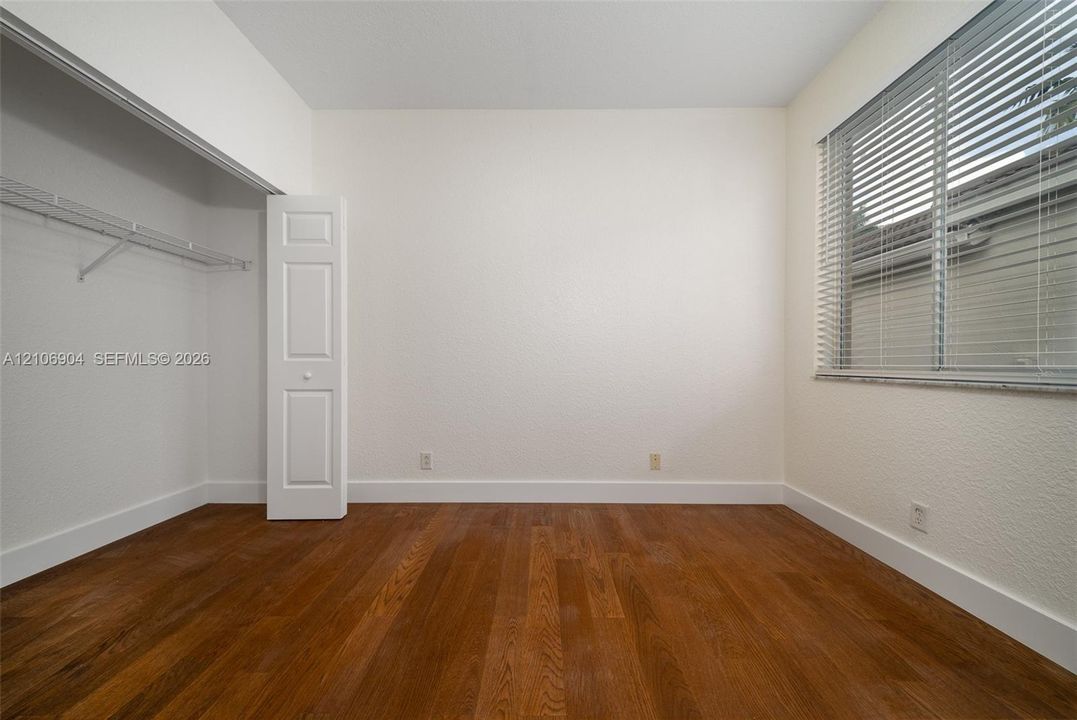 Room featuring wood-finish flooring, a window with horizontal blinds, and a built-in closet with a panel door
