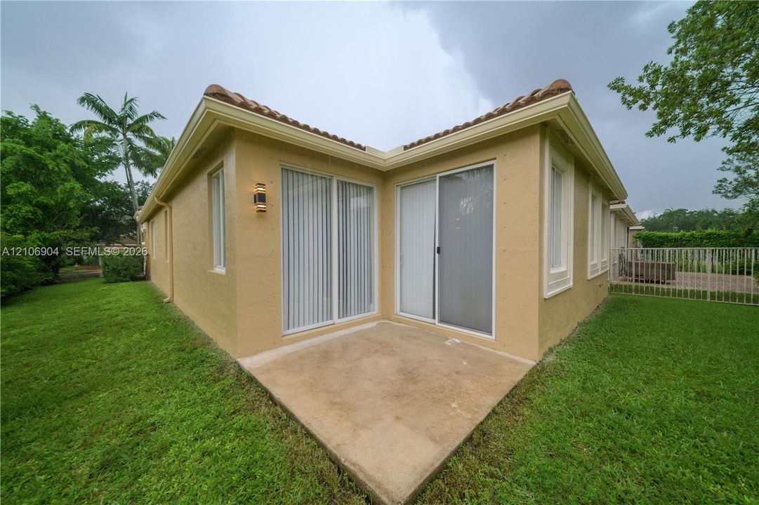 Stucco exterior with a tiled roof, concrete patio, dual sliding glass doors, and exterior wall-mounted lighting