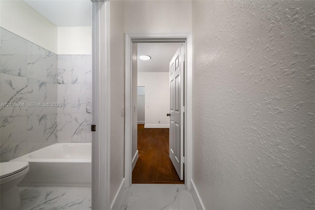 Bathroom featuring large-format tile flooring and wall-surround, integrated bathtub, and wood-finish flooring in the additional room