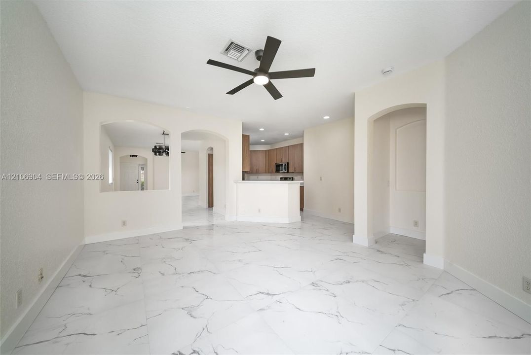 Large-format white tile flooring with veining detail, multi-blade ceiling fan with integrated lighting, arched wall openings, and recessed ceiling lighting