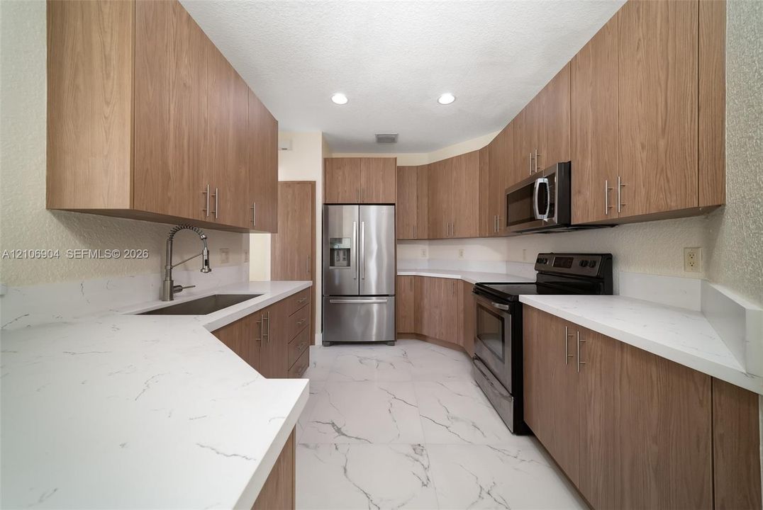 Kitchen featuring wood-finish cabinetry, quartz countertops, stainless steel appliances, and large-format tile flooring