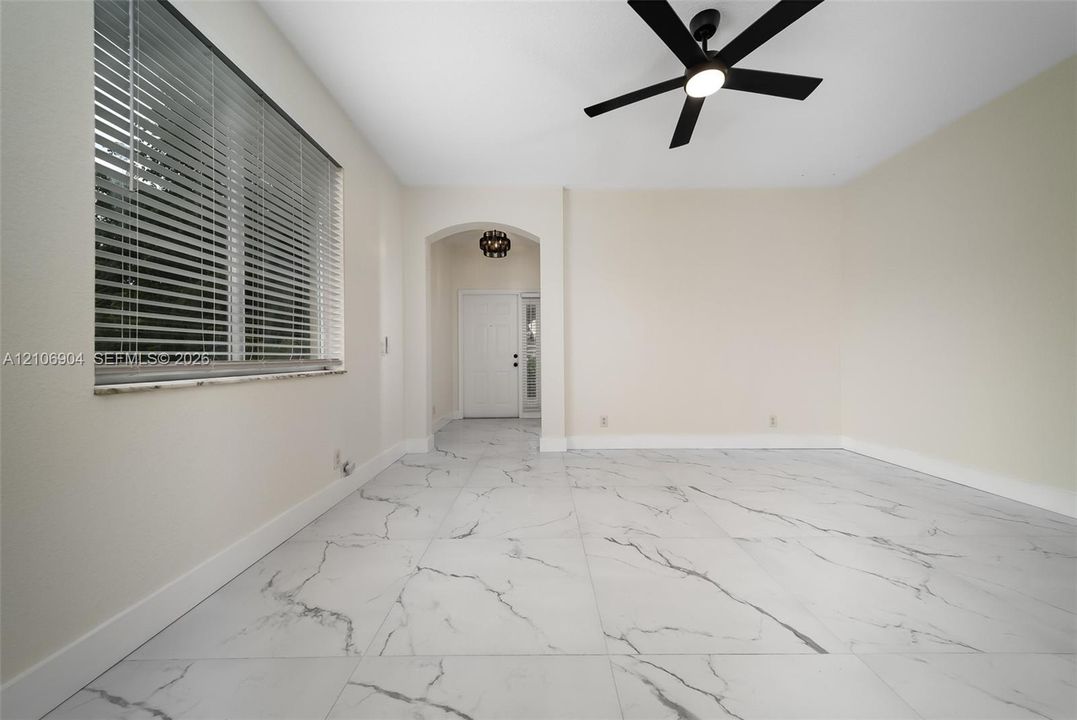 Large-format tile flooring, arched entryway, matte black ceiling fan, and window with built-in blinds