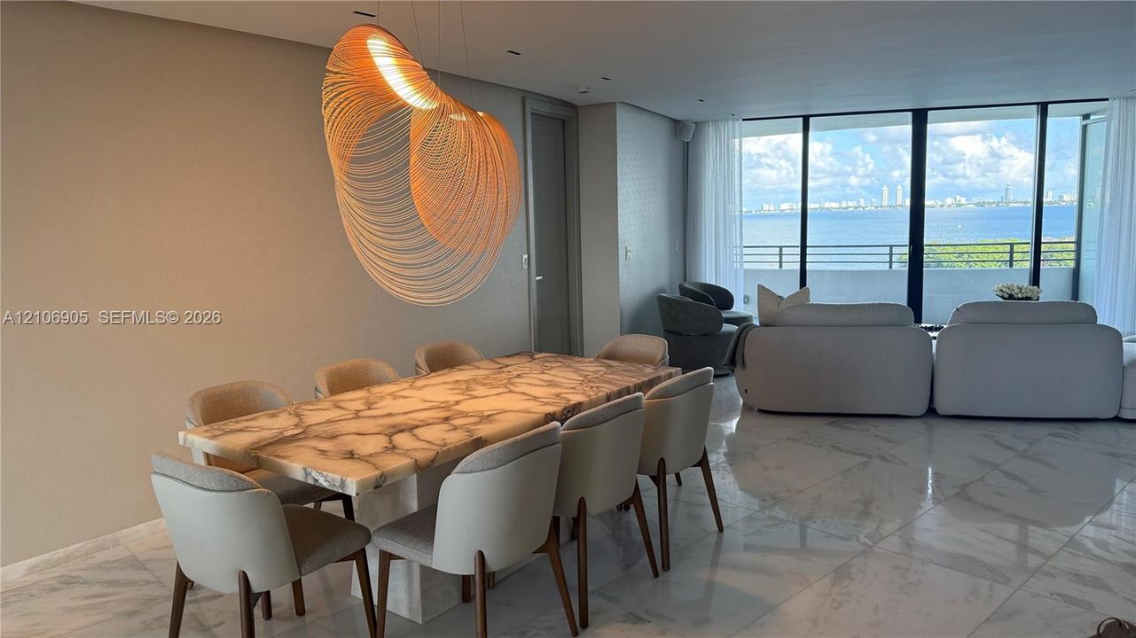 Polished stone flooring, custom sculptural light fixture, and floor-to-ceiling glass wall with access to an expansive balcony