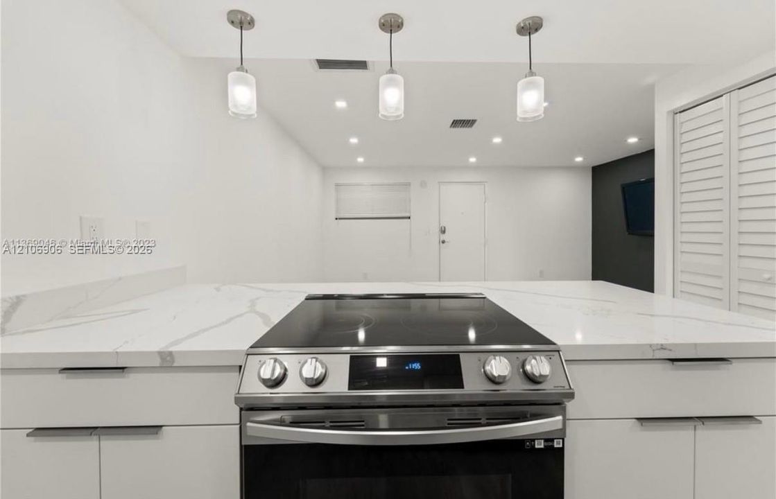 Kitchen featuring a stone-surface countertop, white cabinetry with minimalist hardware, integrated slide-in electric range, and three glass pendant light fixtures