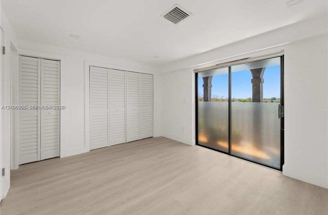 Neutral-toned wood-finish flooring, floor-to-ceiling sliding glass doors, double louvered closet doors, and recessed lighting