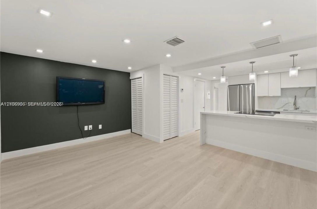 Open-concept interior featuring wood-finish flooring, recessed lighting, white cabinetry, stainless steel appliances, and a quartz-topped peninsula