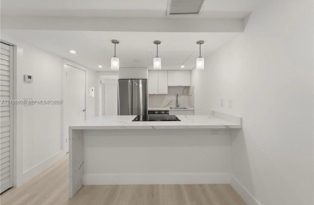 Kitchen featuring a waterfall-edge peninsula with stone-finish countertops, stainless steel appliances, flat-panel white cabinetry, and trio pendant lighting over wood-finish flooring