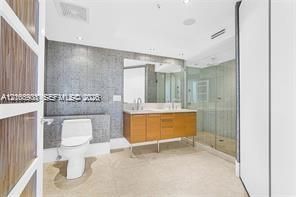 Bathroom featuring a wood-finish floating vanity with a dual-faucet countertop, glass-enclosed shower, mosaic tile wall, and recessed lighting