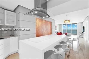 Kitchen featuring a central island with a solid-surface countertop, stainless steel overhead range hood, white cabinetry, wood-finish paneling, and polished flooring