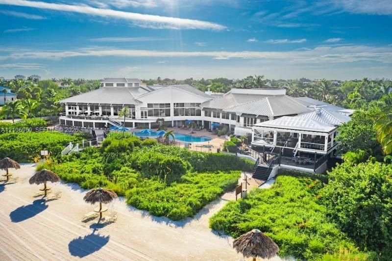 Beachfront estate featuring direct coastal access, an expansive swimming pool, multi-level covered terraces, and mature lush landscaping