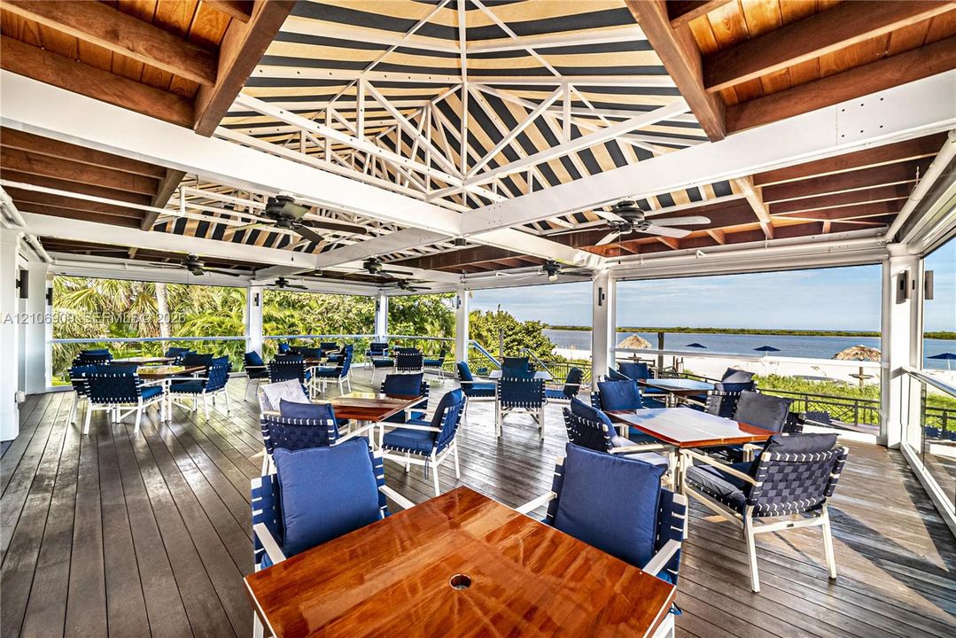 Covered outdoor terrace featuring a wood-plank deck, exposed timber-beam ceiling, overhead fans, and a waterfront backdrop