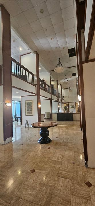 Double-height entry featuring polished stone flooring with decorative inlays, full-height wall mirrors, custom wood-trim detailing, and a mezzanine-level balcony railing