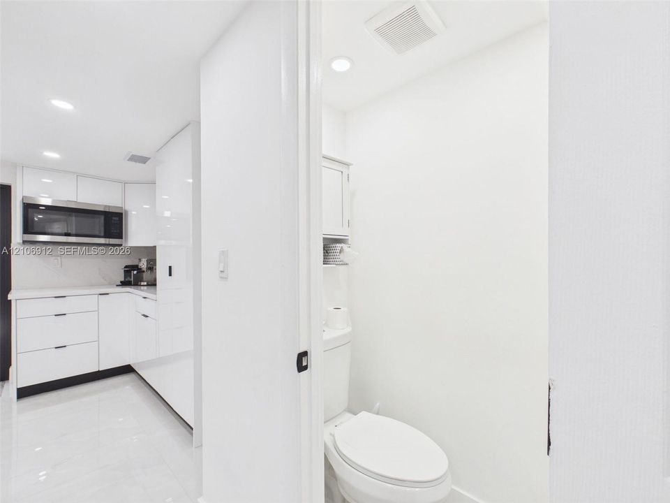 High-gloss cabinetry, stainless steel built-in microwave, stone countertops, recessed lighting, and tile flooring
