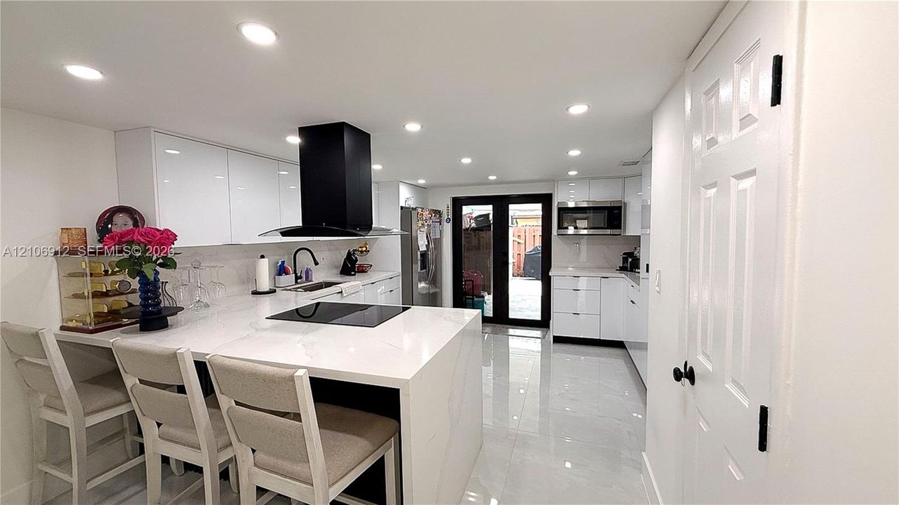 Kitchen featuring high-gloss white cabinetry, a waterfall-edge countertop, black range hood, polished tile flooring, and integrated recessed lighting