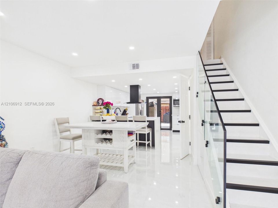 Staircase featuring glass paneling and dark-finished treads, high-gloss tile flooring, recessed ceiling lighting, and a kitchen area with a matte black range hood