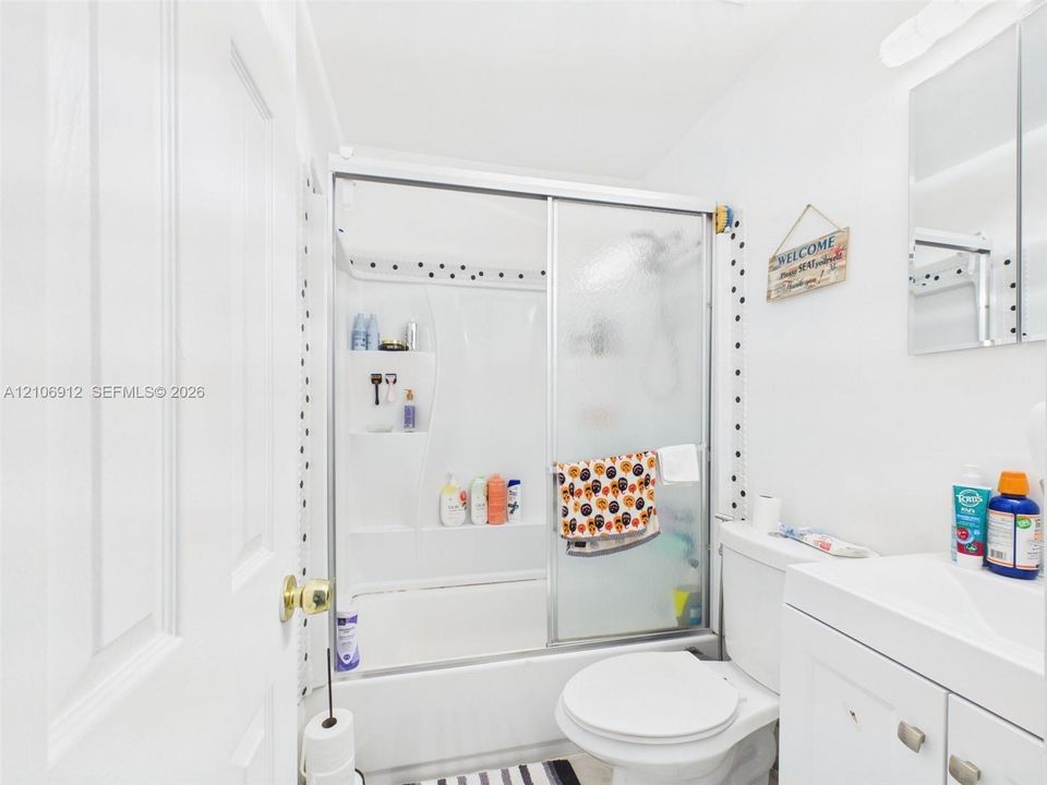 Bathroom featuring a shower and tub combination with sliding glass doors, a white vanity cabinet, and a mirrored medicine cabinet
