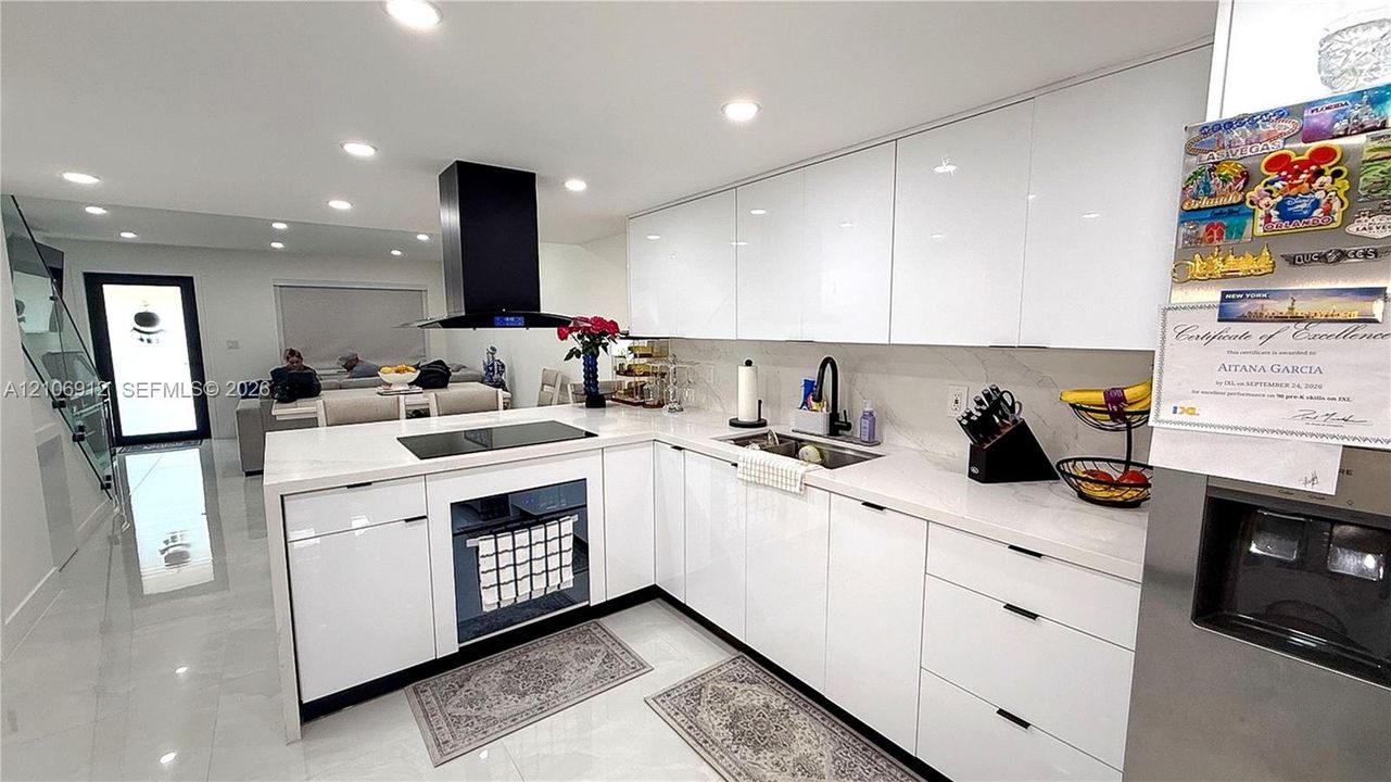 Kitchen featuring high-gloss cabinetry, stone countertops, a large island with an integrated cooktop, a contemporary black chimney-style range hood, and recessed lighting
