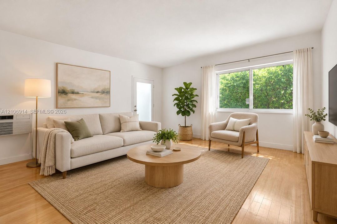 Living space staged featuring wood-finish flooring, a large horizontal window with natural light, and a dedicated wall-mounted air conditioning unit