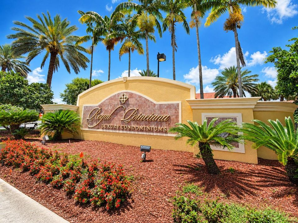 Monolithic property entrance monument with stucco finish, stone-tiled inlay, architectural crown molding, and integrated spotlighting, surrounded by professional desert-style landscaping