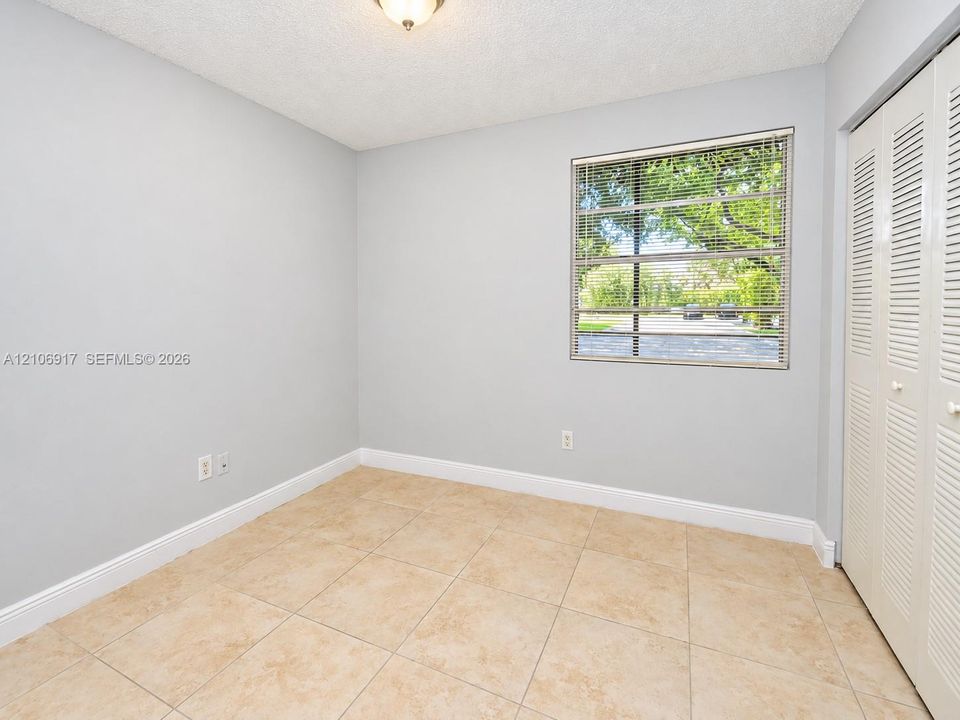 2nd bedroom- Neutral-toned interior featuring large-format ceramic tile flooring, a window with horizontal blinds, and built-in bi-fold closet doors