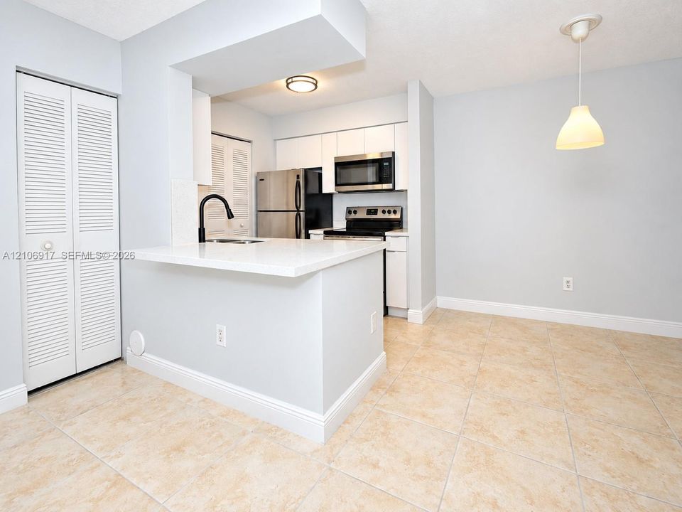 Kitchen featuring white shaker-style cabinetry, quartz countertops, a matte black faucet, stainless steel appliances, and neutral tile flooring