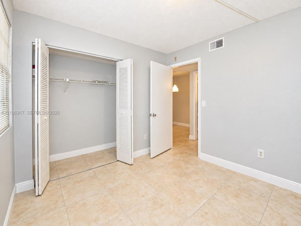 2nd bedroom - Neutral-toned walls paired with large-format tile flooring and a built-in closet featuring louvered bifold doors