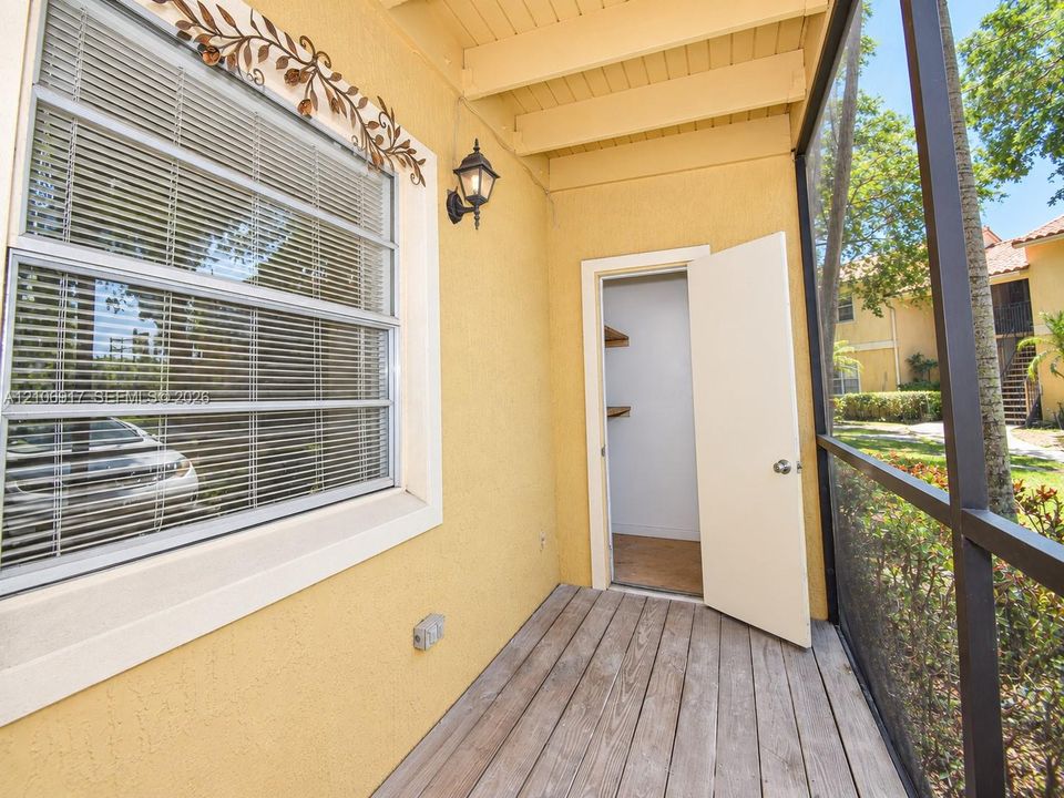 Screened-in outdoor patio featuring wood-finish decking, wall-mounted exterior lighting, and an attached storage closet with built-in shelving