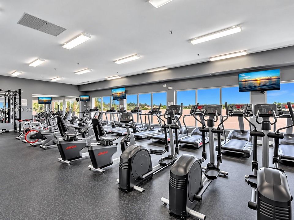 Fitness facility featuring rubberized flooring, expansive windows, multiple overhead LED light fixtures, and wall-mounted televisions
