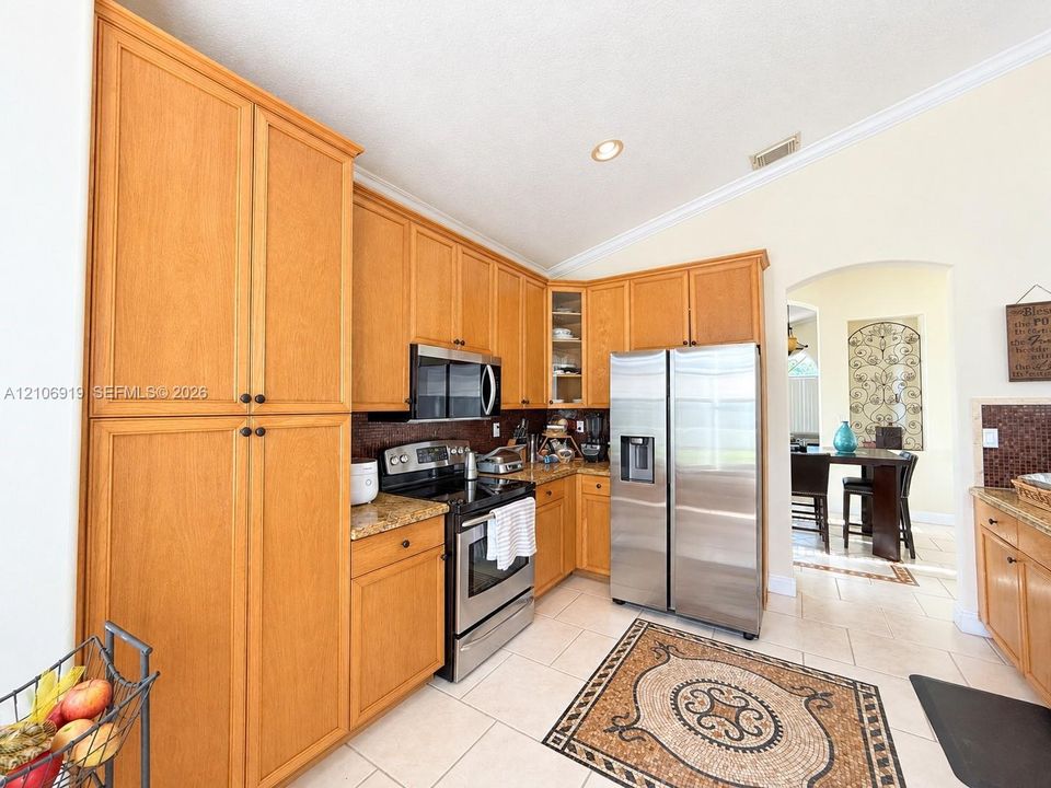 Kitchen featuring natural wood cabinetry, stone countertops, stainless steel appliances, tile flooring, and vaulted ceilings