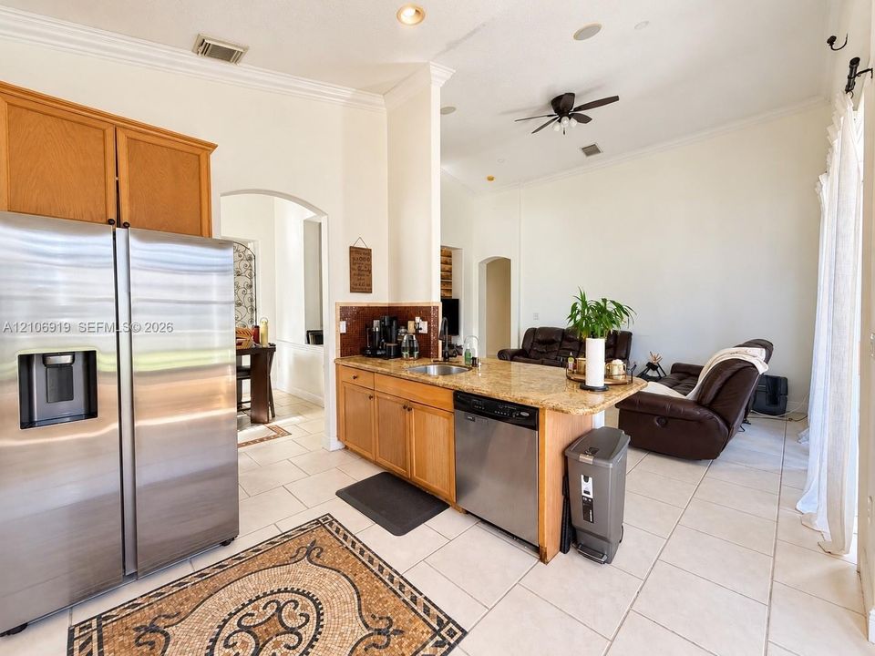 Kitchen featuring stone-finish countertops, stainless steel appliances, wood cabinetry, tile flooring, and arched doorways