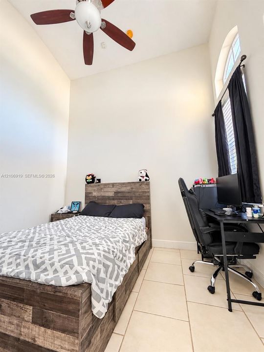 High-ceiling interior space featuring large-format tile flooring, arched window, and a central ceiling fan