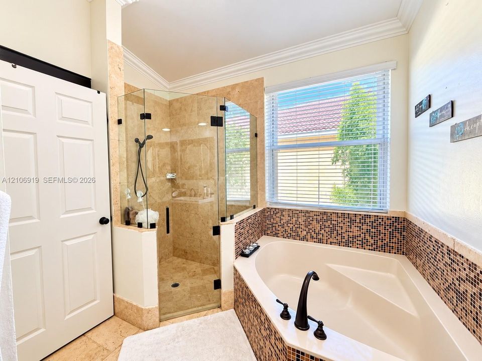 Corner soaking tub with decorative tile surround, glass-enclosed shower with tile finishes, and dual-handle plumbing fixtures