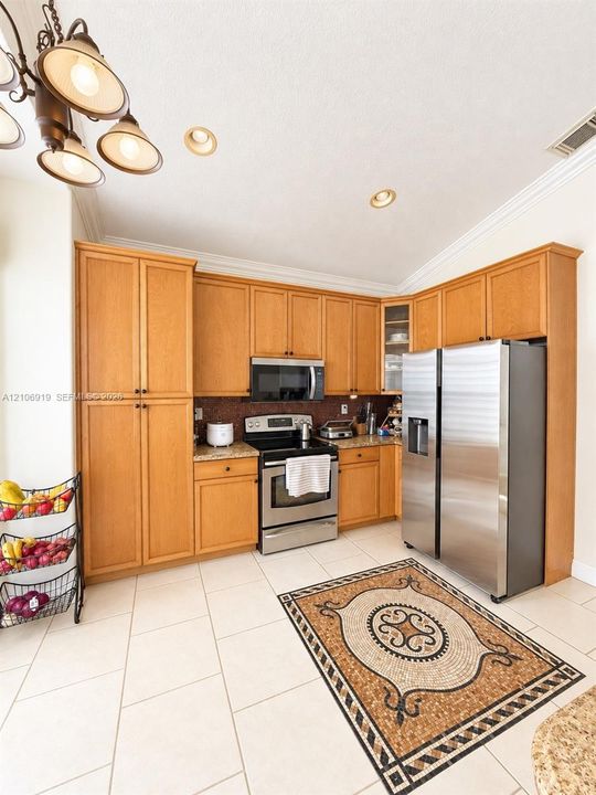 Kitchen featuring light wood cabinetry, stainless steel appliances, tile flooring, crown molding, and a multi-light chandelier