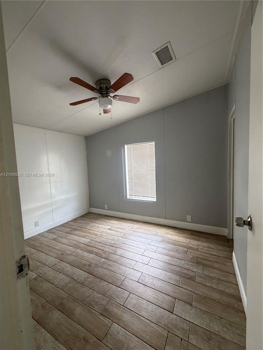 Room featuring vaulted ceilings, wood-finish flooring, and a ceiling fan with integrated lighting