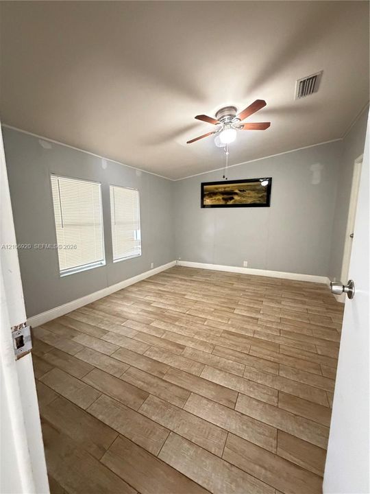 Interior room featuring wood-finish flooring, two windows with integrated blinds, and a ceiling-mounted light fixture with a fan
