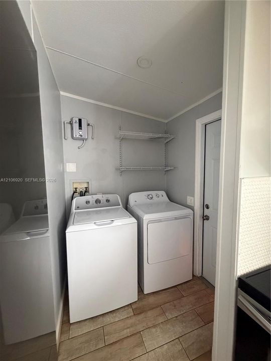 Dedicated laundry area featuring wood-finish flooring, two-tier wall-mounted shelving, and plumbing hookups