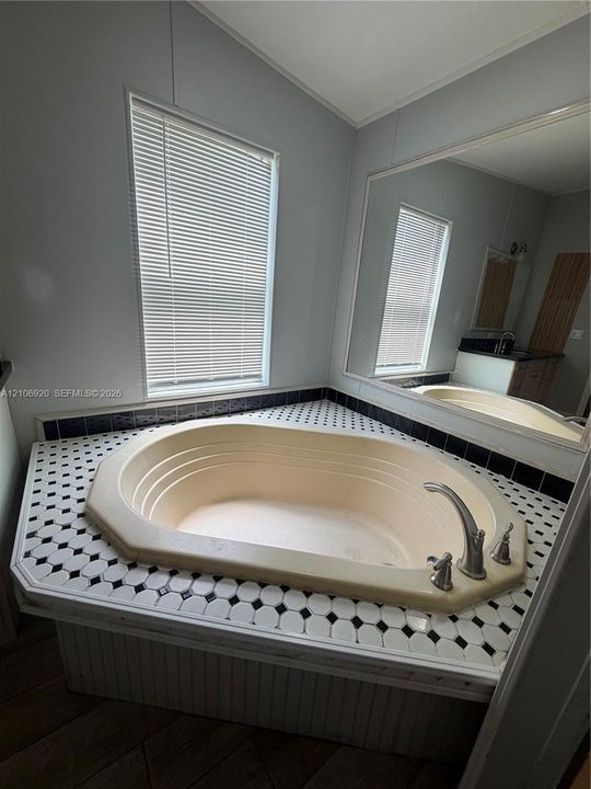 Oversized soaking tub featuring a tiled surround in a black and white geometric pattern, integrated deck-mounted faucet, and a large wall-mounted mirror