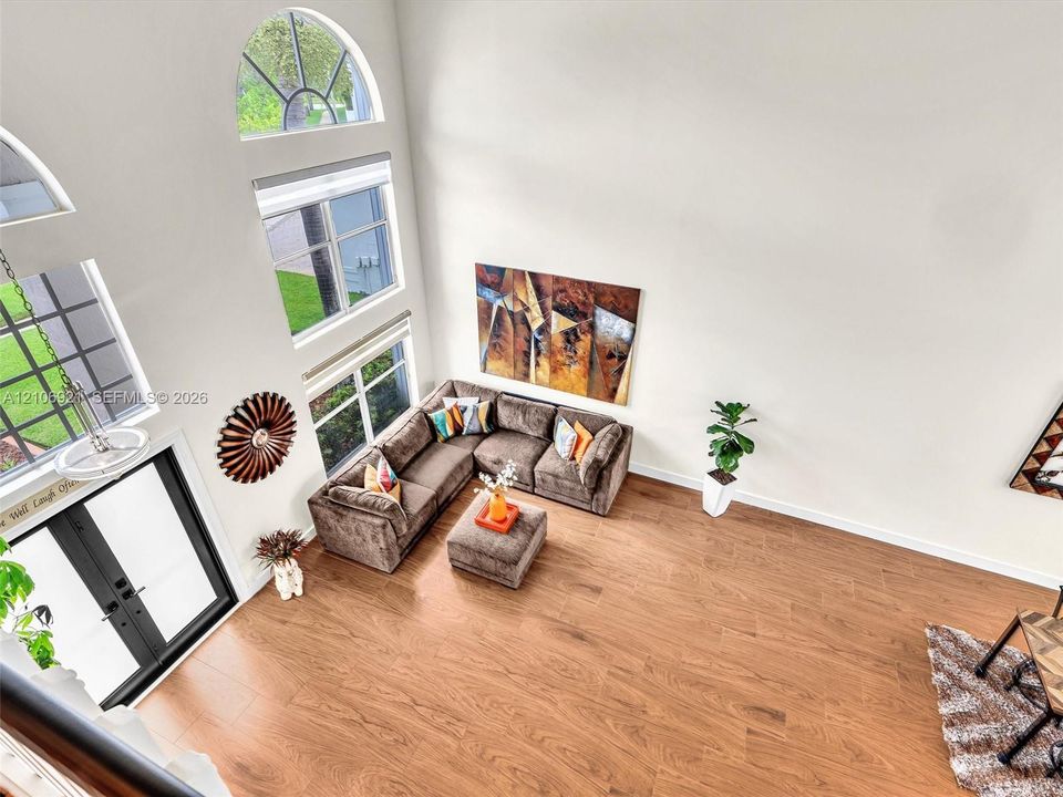 High-ceilinged room featuring wood-finish flooring, a multi-pane arched window, and a modern dual-pane window configuration with a hanging pendant light fixture