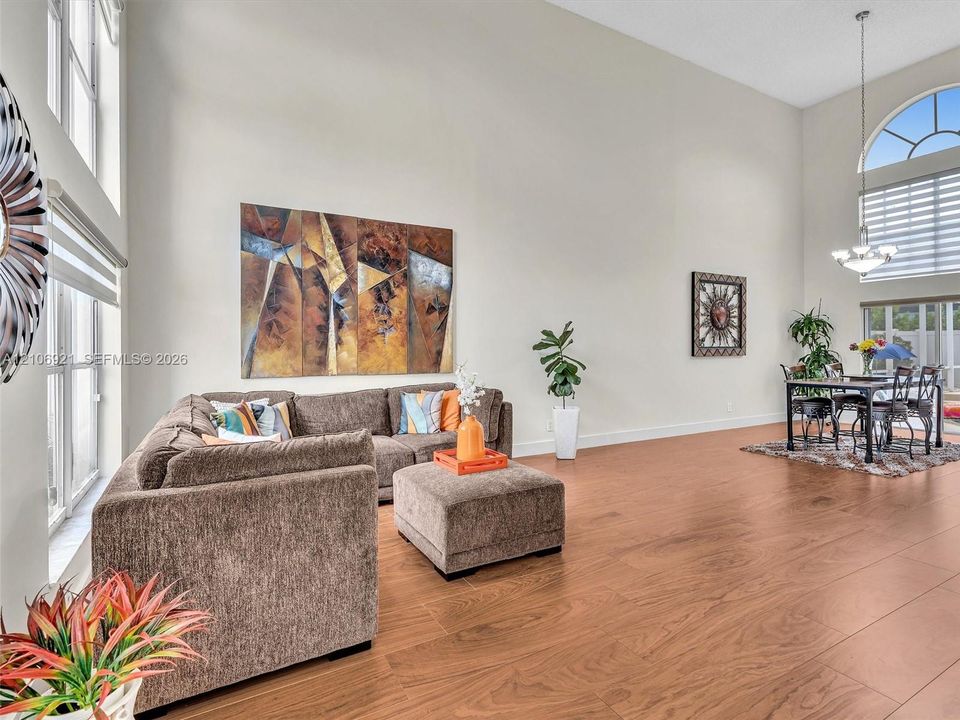 High-ceilinged interior space featuring wood-finish flooring, floor-to-ceiling windows, an arched window, and a multi-light chandelier