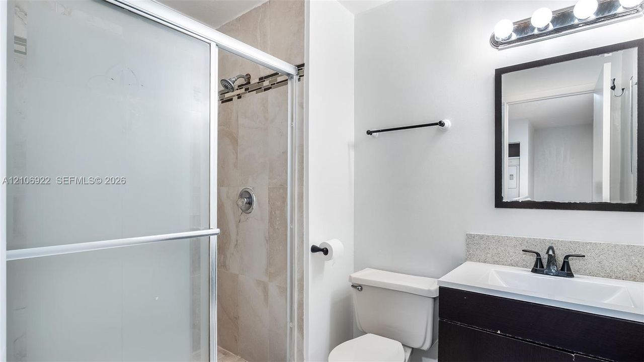 Bathroom featuring a dark wood-finish vanity with a stone countertop, an integrated sink, a framed wall mirror, and a walk-in shower with stone-tile surround and a sliding glass door