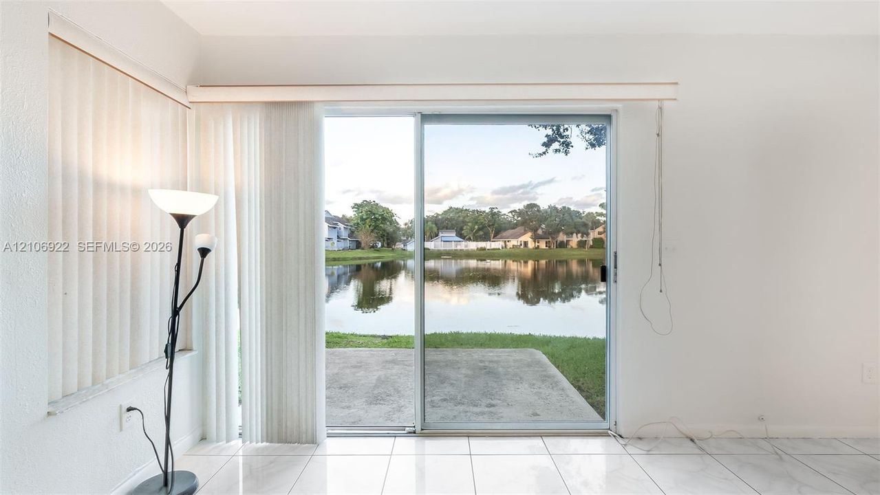 Sliding glass doors opening to a concrete patio, light-colored tile flooring, and water frontage