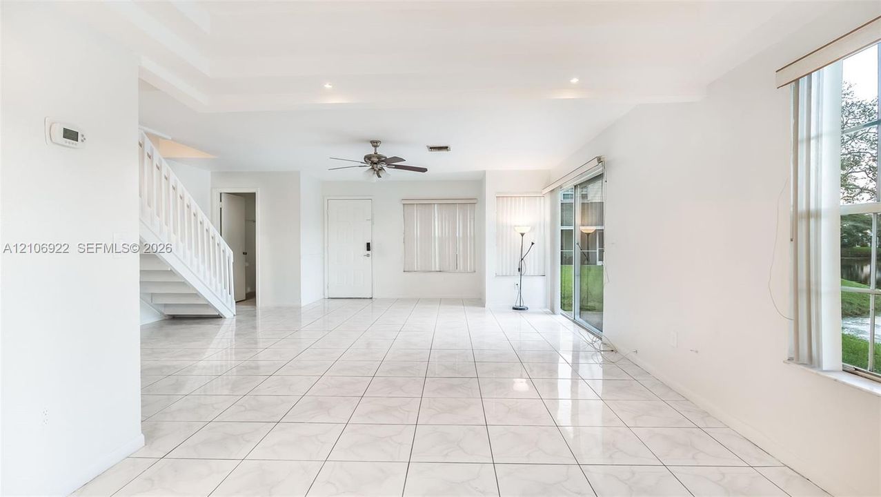 Open-concept interior featuring oversized tile flooring, tray ceilings, recessed lighting, a staircase with white balusters, and sliding glass doors