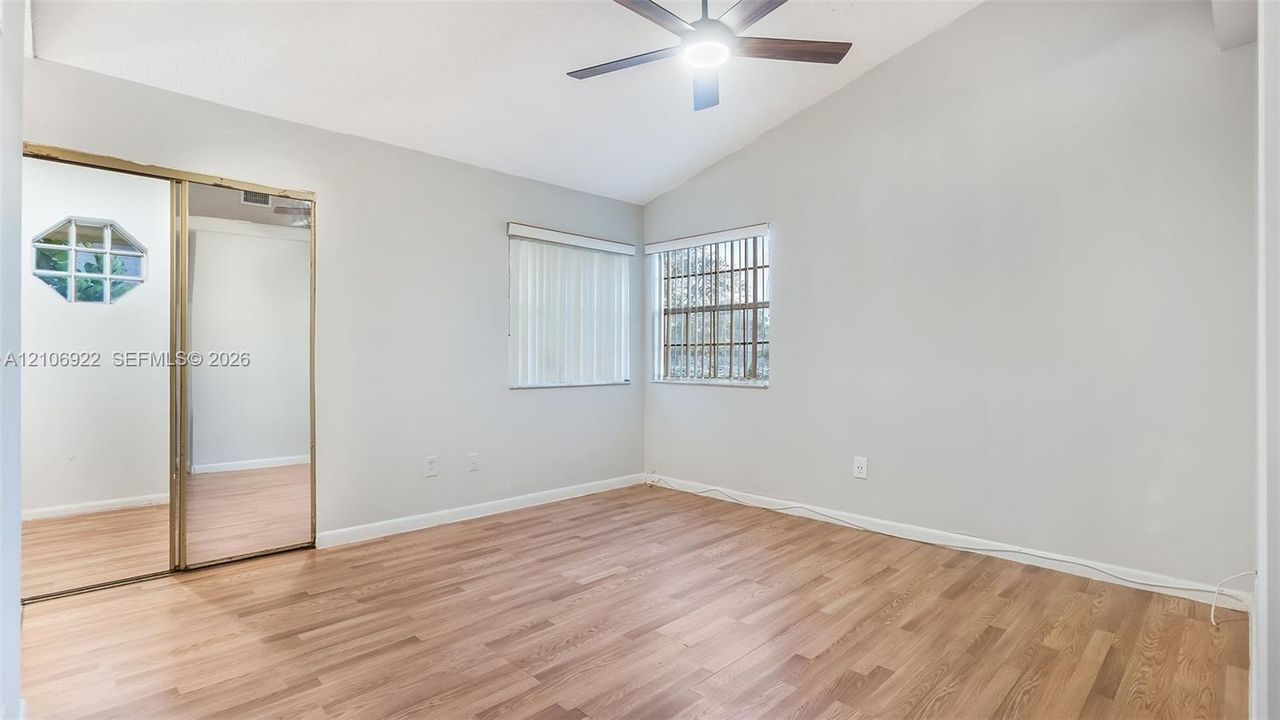 Vaulted ceilings, wood-finish flooring, sliding mirrored closet doors, and a ceiling fan with integrated lighting