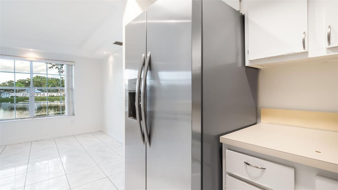 Stainless steel side-by-side refrigerator, white cabinetry, solid-surface countertops, grid-pattern windows, and light-toned tile flooring