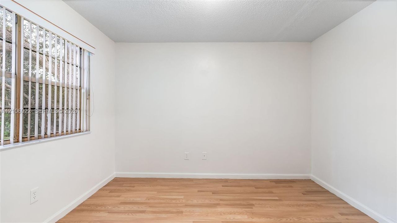 Neutral-toned interior space featuring wood-finish flooring and a single-pane window with vertical blinds