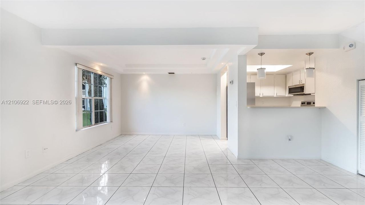 Open-concept interior featuring white tile flooring, recessed ceiling lighting, a pass-through breakfast bar, and white cabinetry