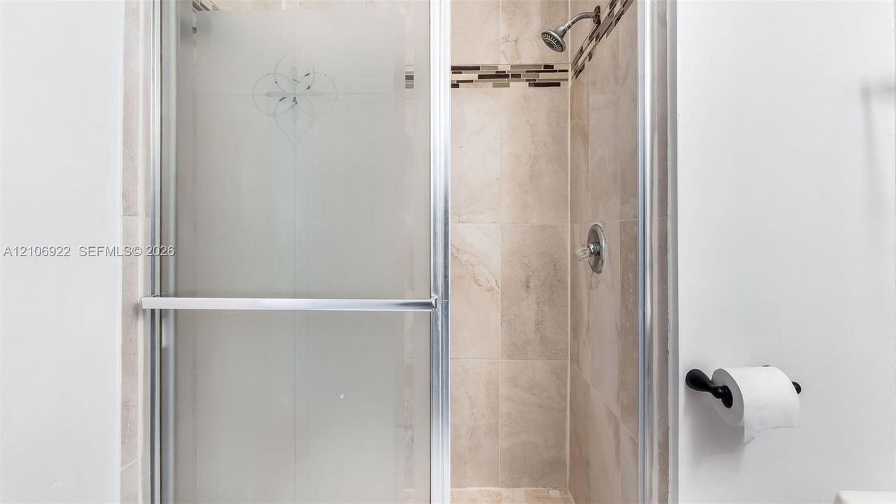 Shower stall featuring a framed glass door with frosted inlay, stone-finish wall tile, a decorative glass mosaic tile accent border, and a chrome shower fixture