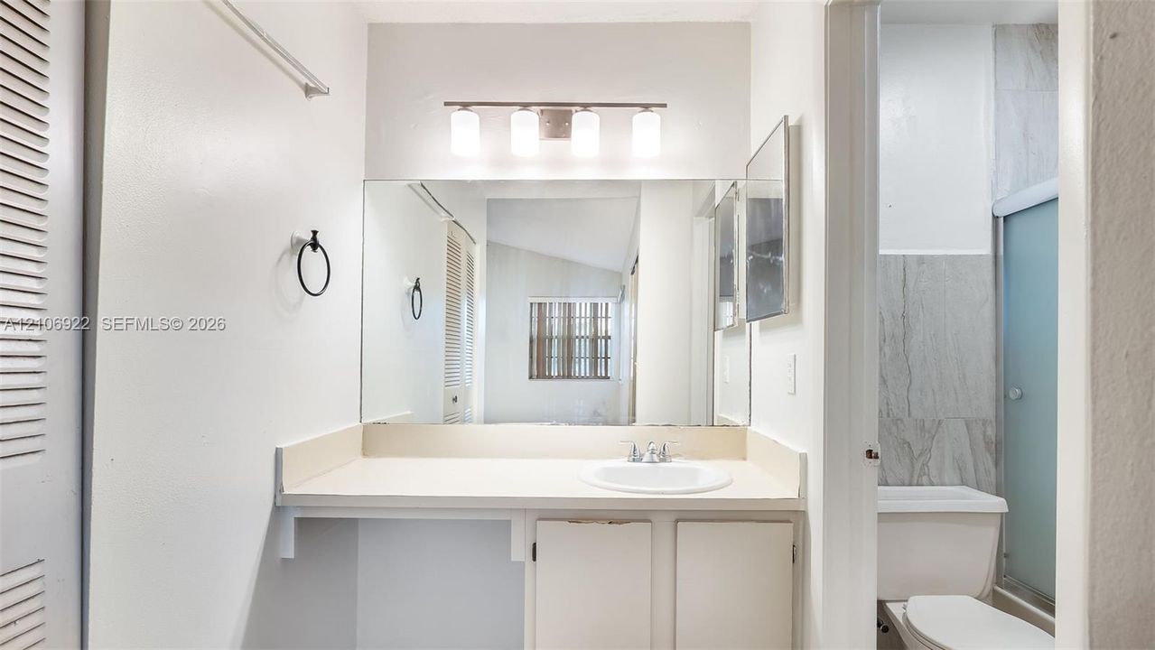 Bathroom vanity featuring a solid surface countertop with an integrated basin, a large wall-mounted mirror, a four-light fixture, and stone-finish shower surround